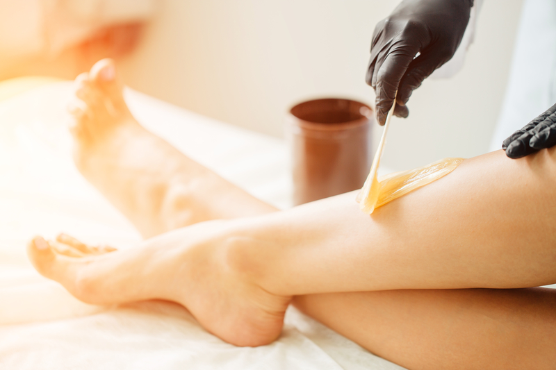 close up Beautician waxing female legs in spa center